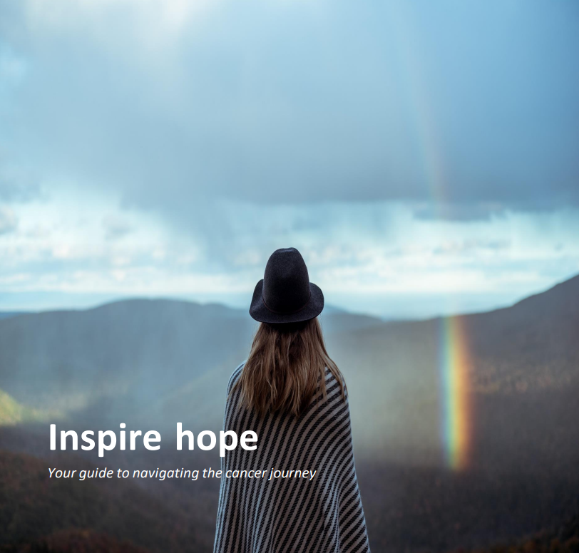 a woman with long light brown hair in a black floppy hat and a striped poncho/blanket stands with her back to the camera looking out on a valley. The sky is overcast and its misty. There's a natural rainbow in the right side of the image. The words "Inspire hope, your guide to navigating the cancer journey" is in the foreground.