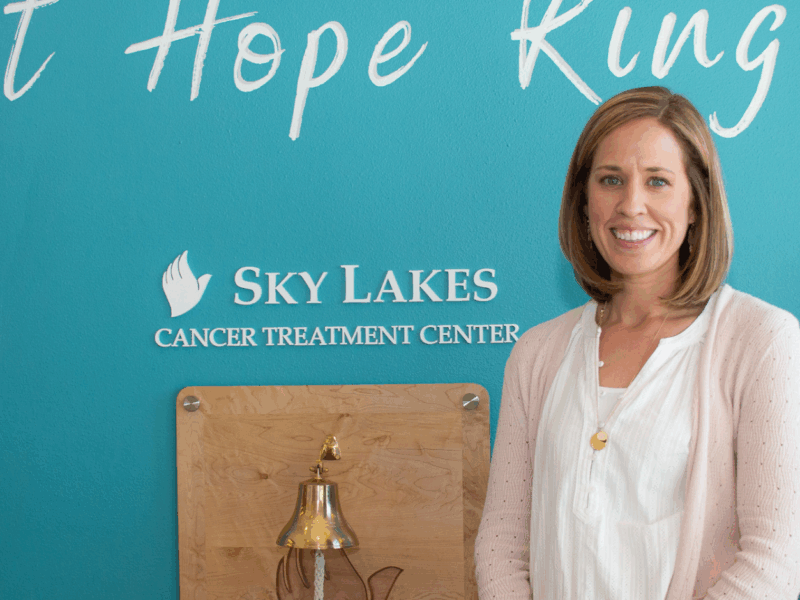 Nurse Hannah Sonerholm standing in front of a blue wall that says "let hope Ring' and "Sky Lakes Cancer Treatment Center"