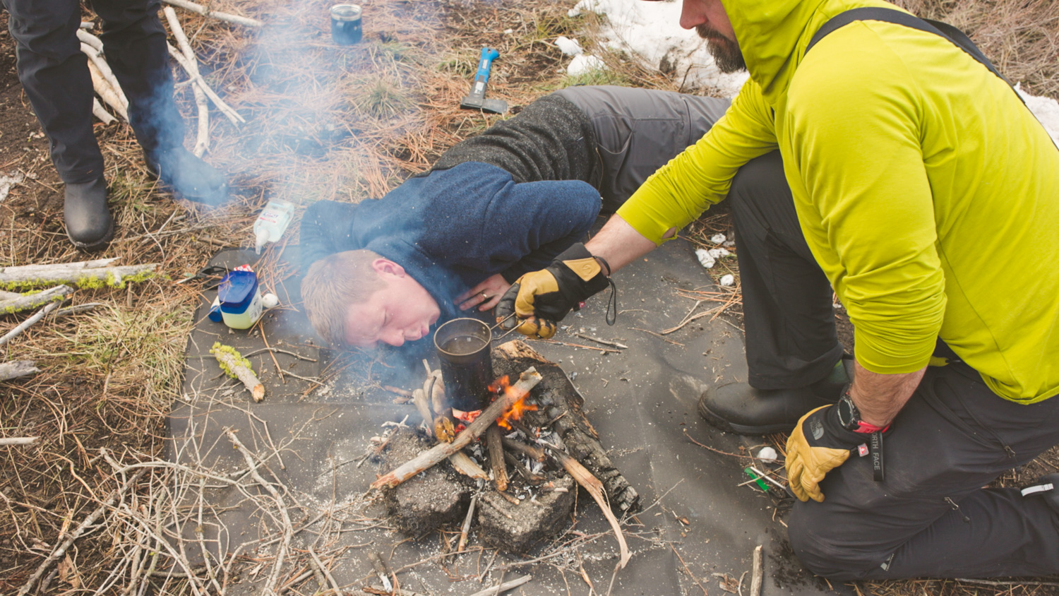 Dr. Rogers on the ground helping a campfire fire start by blowing on the flames